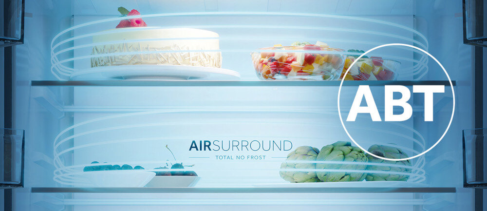 Wnętrze lodówki z dwoma półkami, na których znajdują się różne produkty spożywcze. Widoczny jest napis \'AIR SURROUND TOTAL NO FROST\' oraz duże logo \'ABT\'.