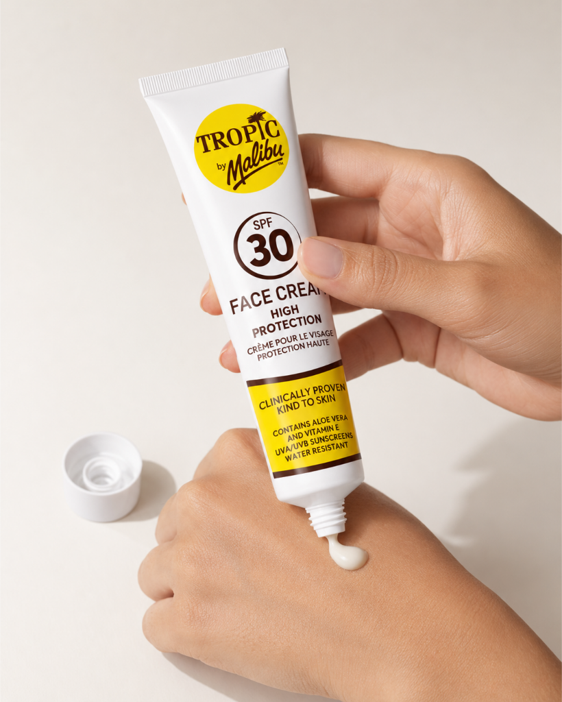 Osoba wyciska krem z tubki oznaczonej jako \'Tropic by Malibu SPF 30 Face Cream High Protection\' na dłoń. Tubka jest biała z żółtym logo i czarnym tekstem, a obok leży otwarta zakrętka.