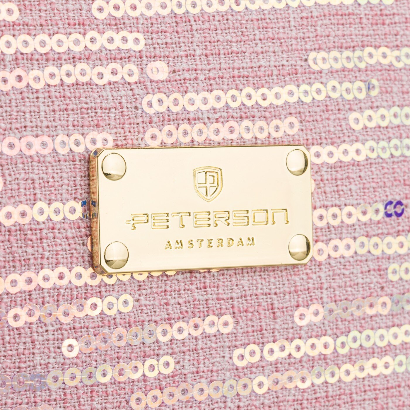Różowy materiał pokryty cekinami z metalową plakietką z napisem \'PETERSON AMSTERDAM\'.