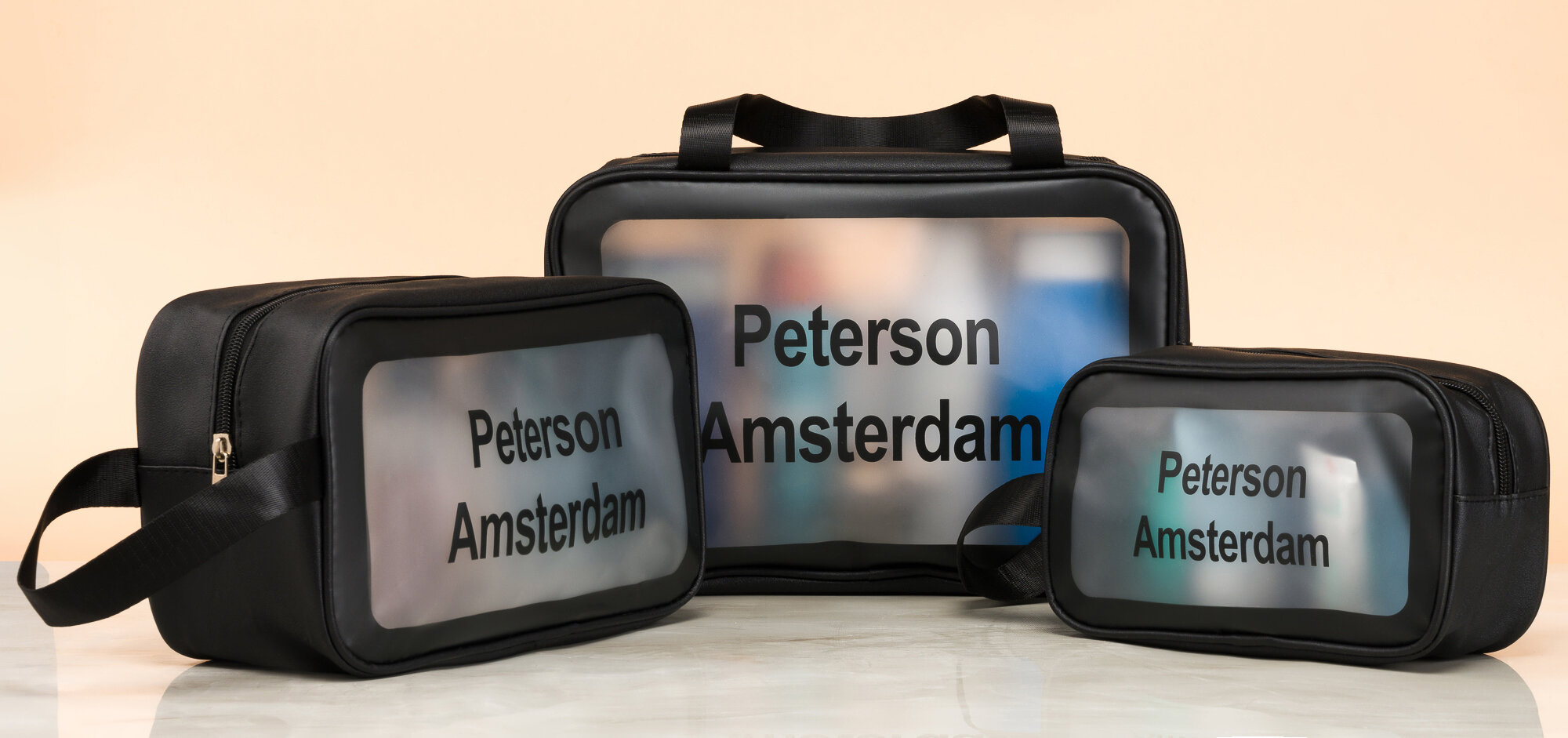 Trzy czarne, przezroczyste saszetki podróżne z napisem \'Peterson Amsterdam\'.