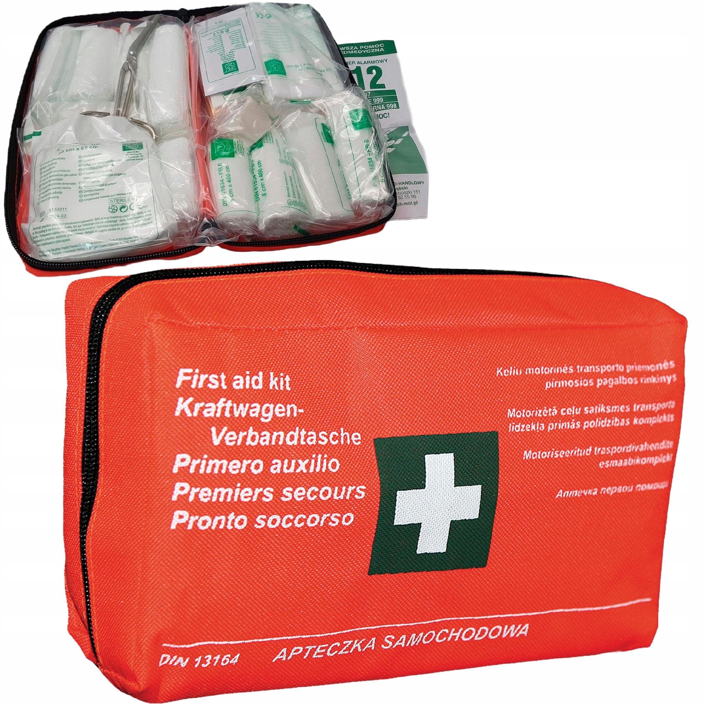 Na obrazie widoczna jest czerwona apteczka samochodowa z białym krzyżem i napisami w kilku językach, w tym \'First aid kit\' i \'APTECZKA SAMOCHODOWA\'. Wnętrze apteczki zawiera różne materiały opatrunkowe zapakowane w przezroczyste woreczki.