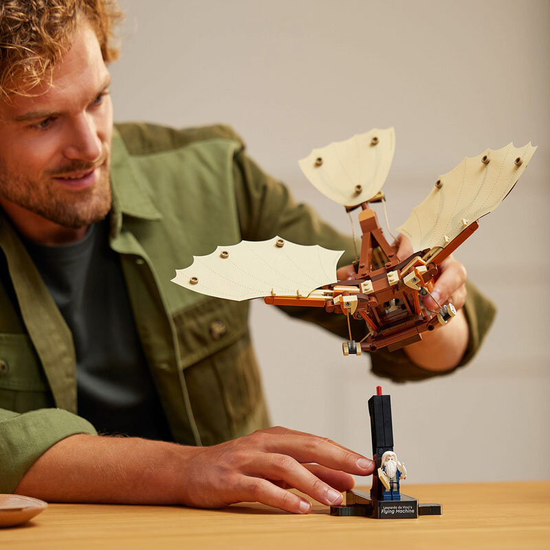 Osoba trzyma model maszyny latającej zbudowany z klocków, przypominający projekt Leonarda da Vinci. Na podstawce widoczny jest napis: \'Flying Machine\'.