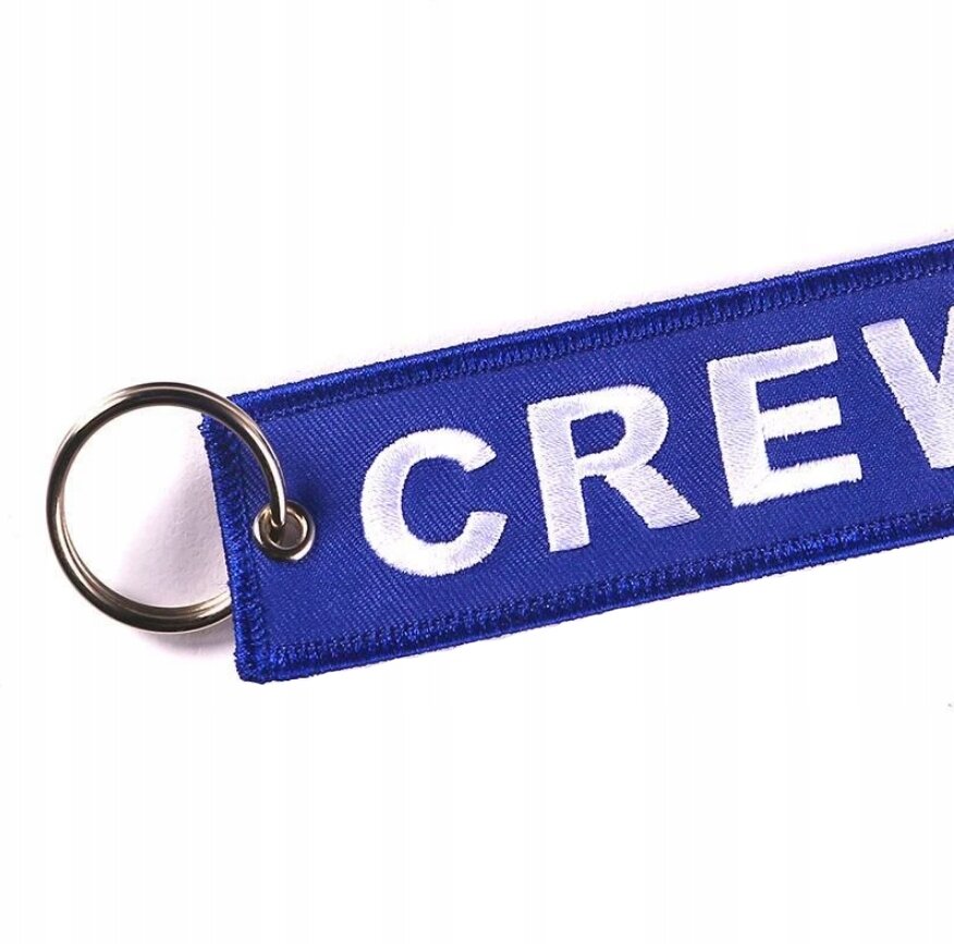 Niebieski brelok z napisem \'CREW\' w białym kolorze, przymocowany do metalowego kółka.