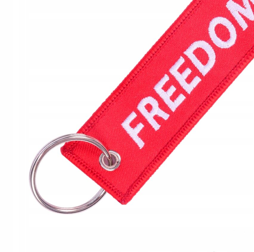 Czerwony brelok z napisem \'FREEDOM\' w białym kolorze, posiada metalowe kółko do zawieszenia kluczy.