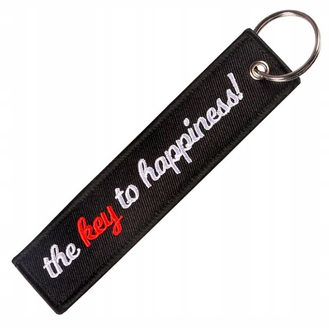 Czarny brelok z napisem \'the key to happiness!\', gdzie słowo \'key\' jest w kolorze czerwonym. Brelok ma metalowe kółko do zawieszania kluczy.