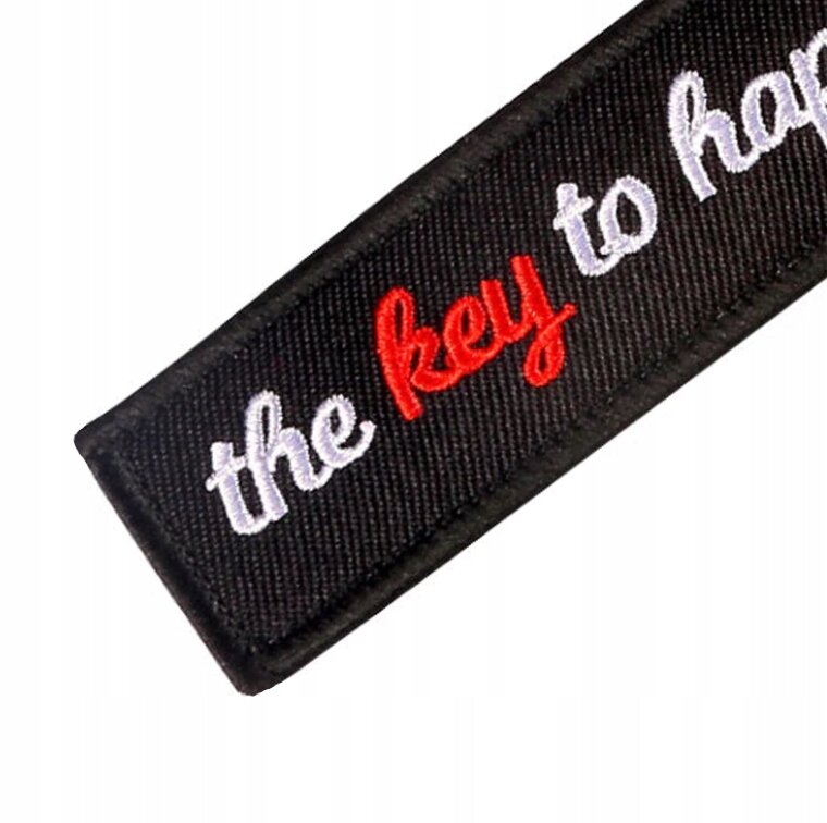 Czarny brelok z napisem \'the key to happiness\' w kolorach białym i czerwonym.