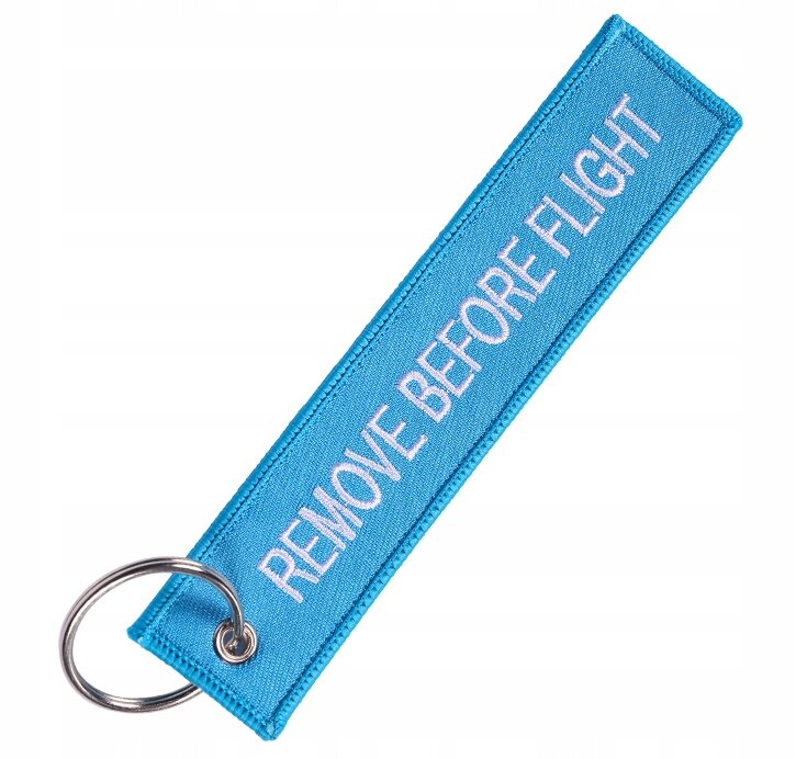 Niebieski brelok z napisem \'REMOVE BEFORE FLIGHT\' i metalowym kółkiem do zawieszania.