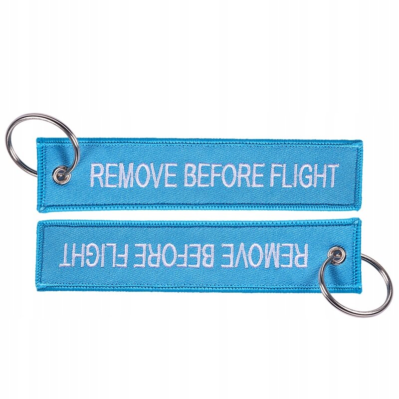 Na obrazie widoczne są dwa niebieskie breloki z napisem \'REMOVE BEFORE FLIGHT\', każdy z metalowym kółkiem do zawieszenia.