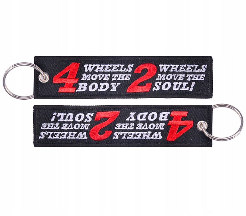 Na obrazie widoczne są dwa czarne breloki z metalowymi kółkami, z napisem \'4 WHEELS MOVE THE BODY 2 WHEELS MOVE THE SOUL!\' w kolorze białym i czerwonym.