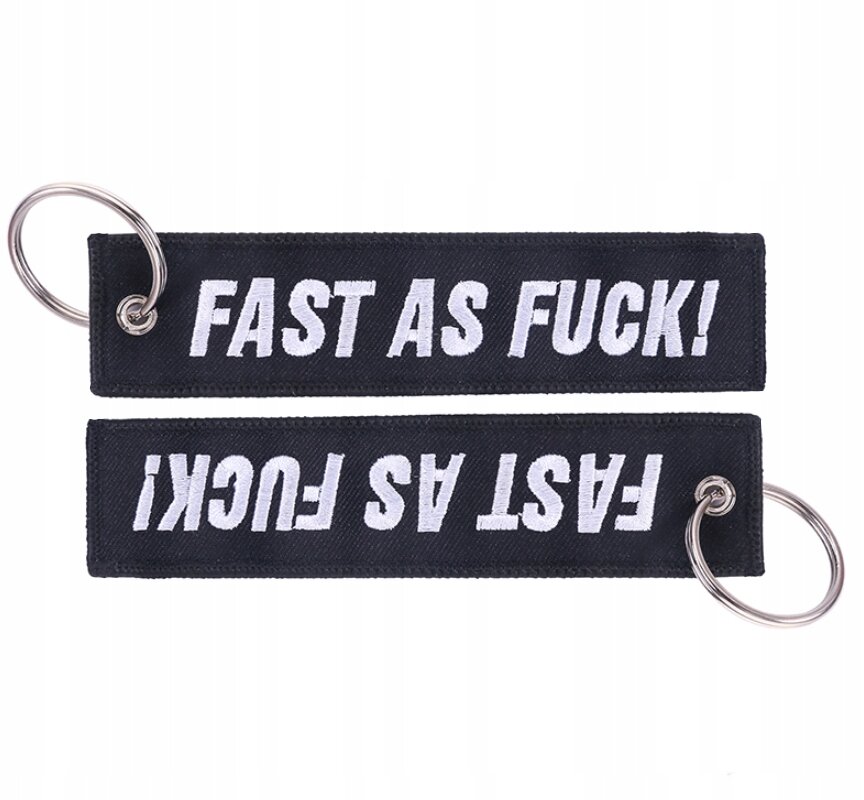 Na obrazie widoczne są dwa czarne breloki z metalowymi kółkami, z białym napisem \'FAST AS FUCK!\' po obu stronach.