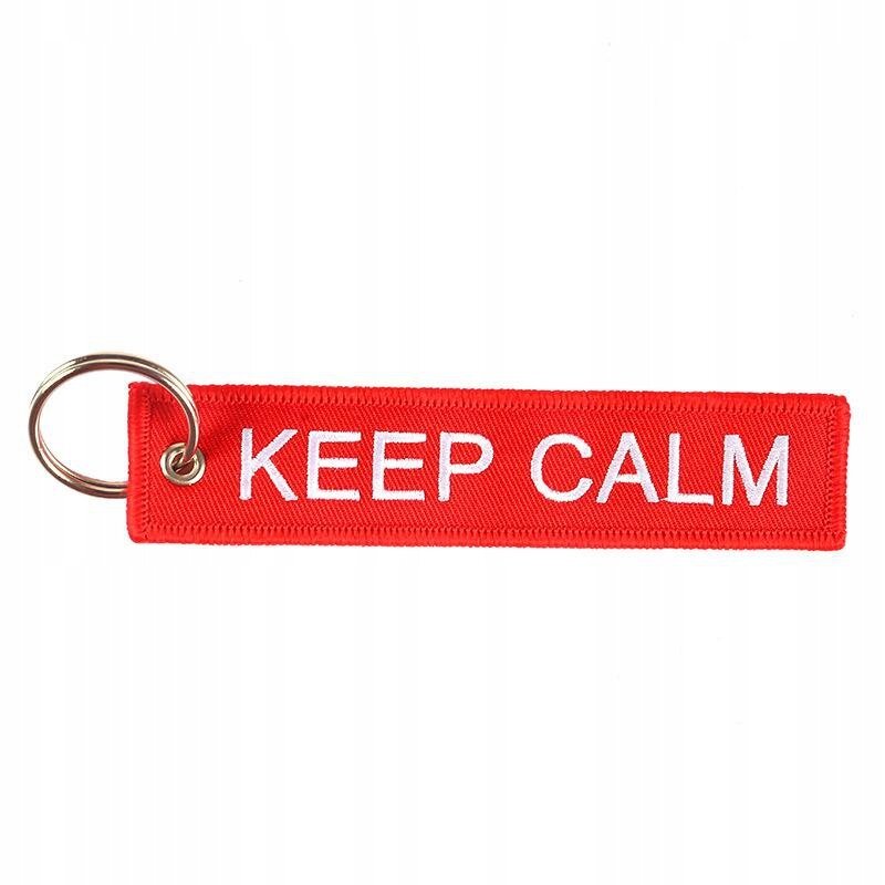 Czerwony brelok z napisem \'KEEP CALM\' w białym kolorze, posiada metalowe kółko do zawieszenia kluczy.