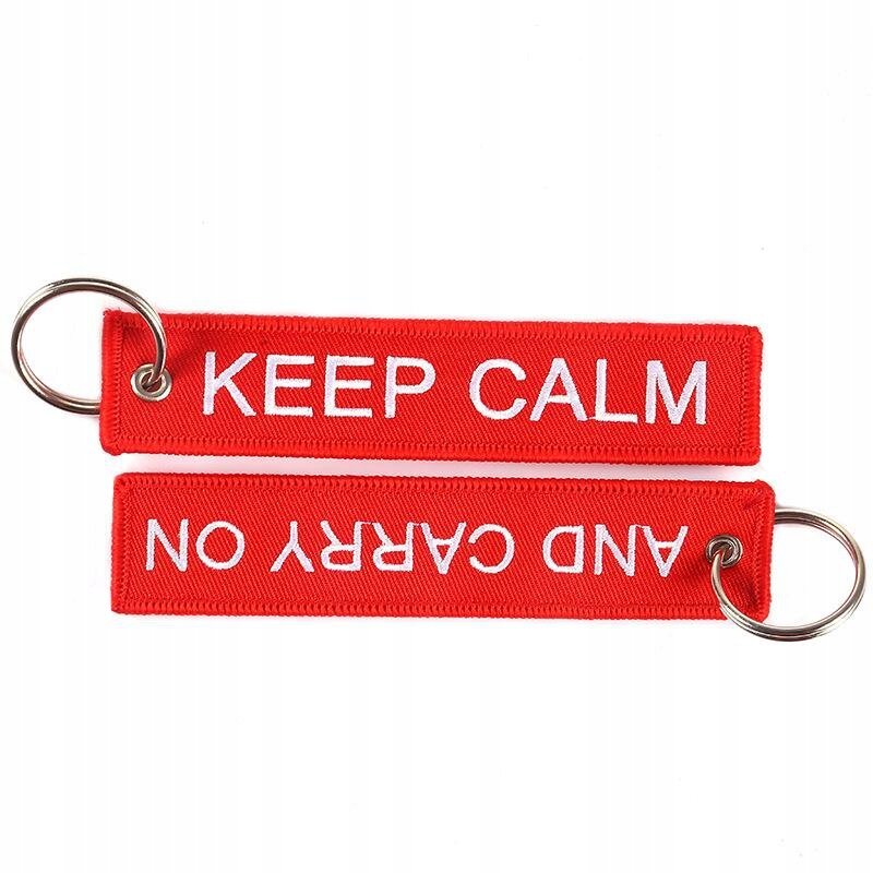 Czerwony brelok z białym napisem \'KEEP CALM\' na jednej stronie i \'AND CARRY ON\' na drugiej stronie, z metalowym kółkiem do zawieszania kluczy.