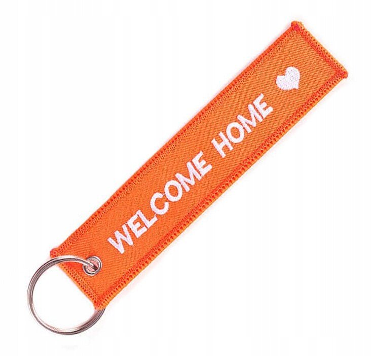 Pomarańczowy brelok z napisem \'WELCOME HOME\' i białym sercem, posiada metalowe kółko do zawieszania kluczy.