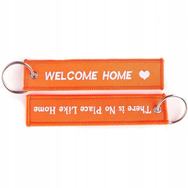 Dwa pomarańczowe breloki z metalowymi kółkami, na jednym napis \'WELCOME HOME\' z sercem, na drugim \'There is NO Place Like Home\'.