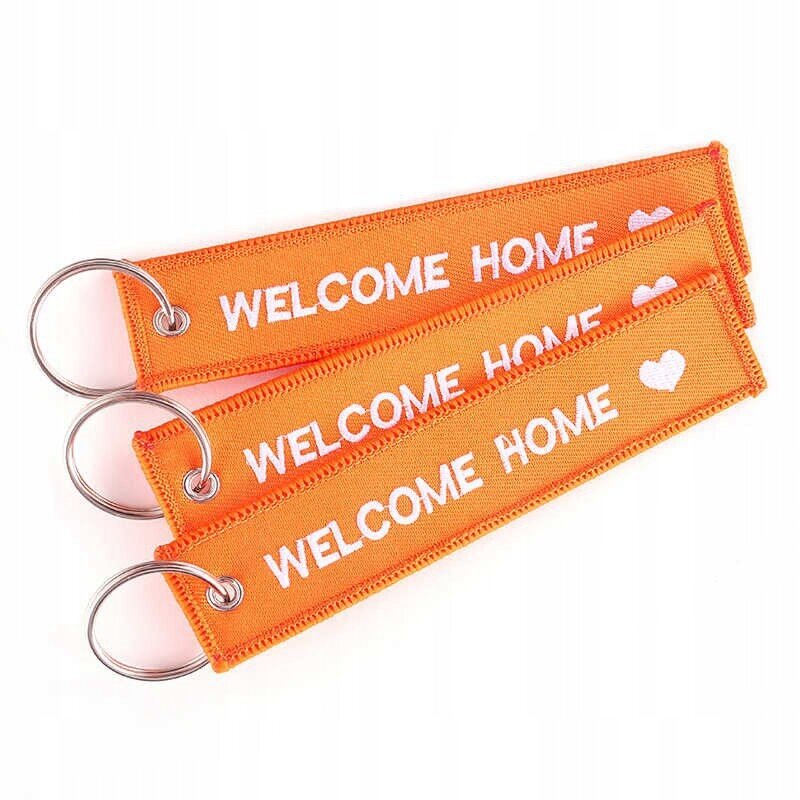 Trzy pomarańczowe breloki z napisem \'WELCOME HOME\' i białym sercem, każdy z metalowym kółkiem do kluczy.