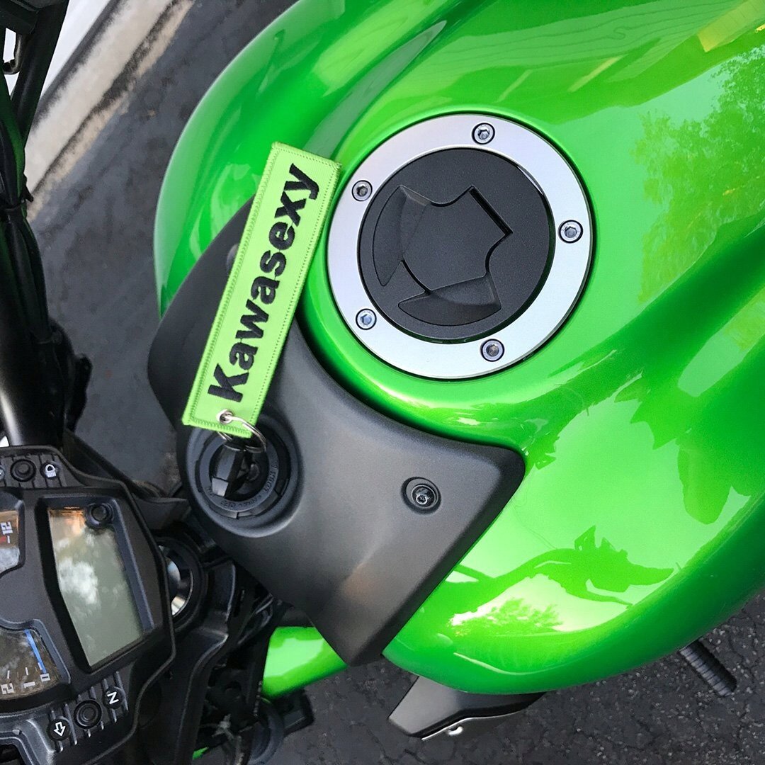 Zielony motocykl z widocznym wlewem paliwa i brelokiem z napisem \'Kawasexy\'.