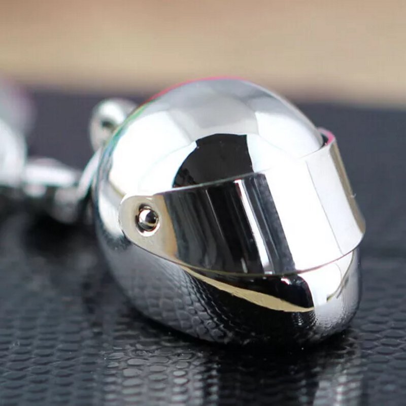 Srebrny metalowy brelok w kształcie kasku z gładką, błyszczącą powierzchnią. Kask posiada wizjer i jest przymocowany do łańcuszka.