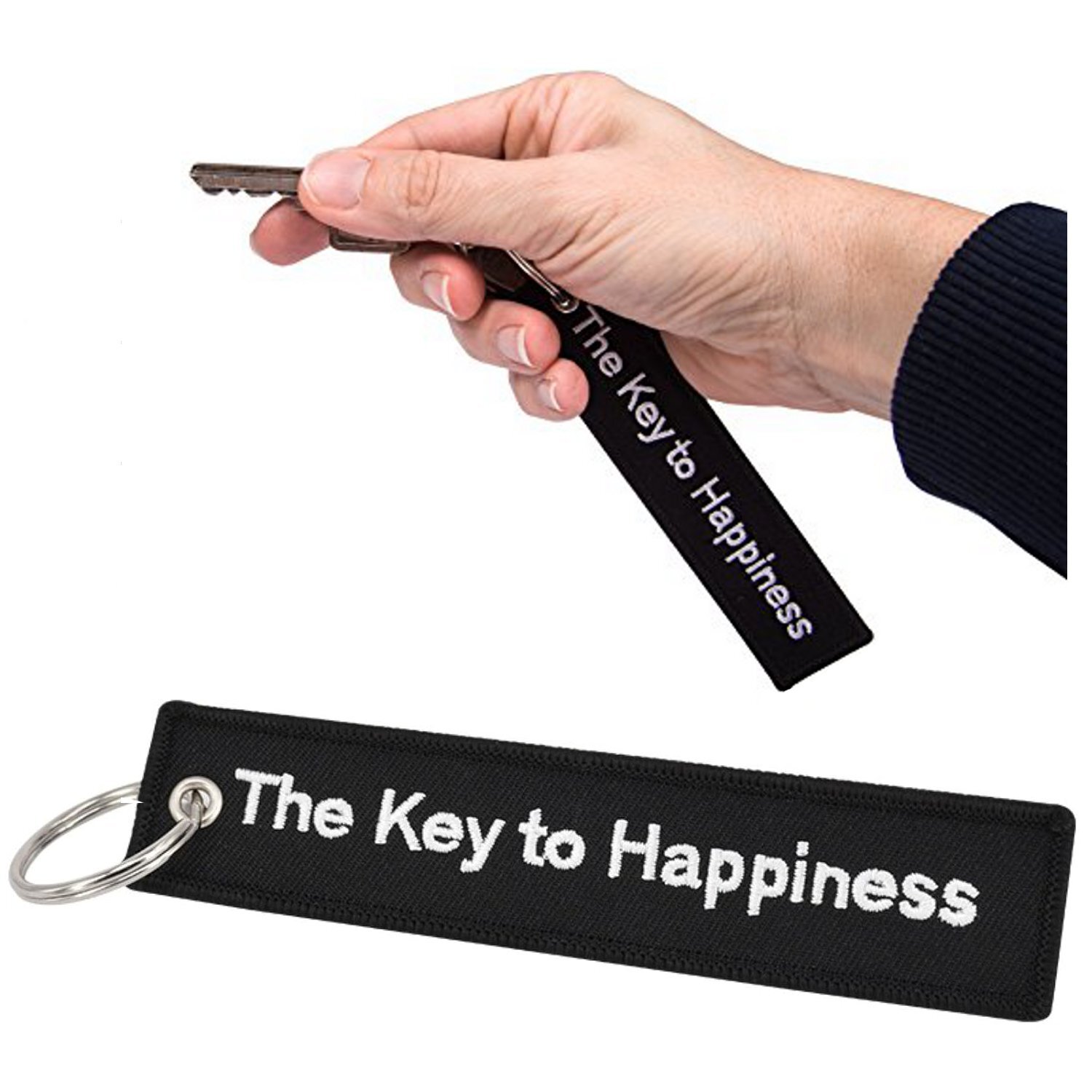 Osoba trzyma brelok do kluczy z napisem \'The Key to Happiness\'. Brelok jest czarny z białym tekstem i posiada metalowe kółko na klucze.
