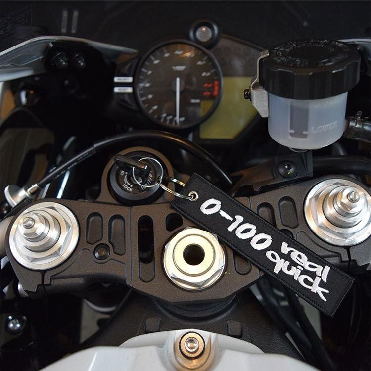 Na zdjęciu widoczny jest kokpit motocykla z brelokiem do kluczy z napisem \'0-100 real quick\'.