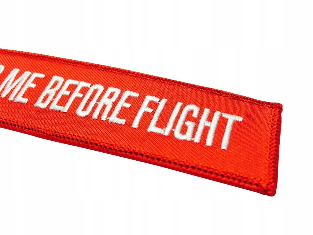 Czerwony brelok z białym napisem \'KISS ME BEFORE FLIGHT\'.