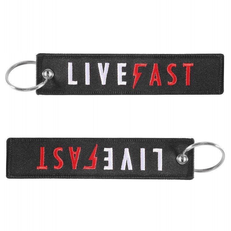 Czarny brelok z napisem \'LIVE FAST\' w kolorach białym i czerwonym, z metalowym kółkiem do zawieszania. Napis jest widoczny z obu stron breloka.