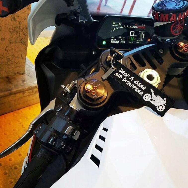 Zdjęcie przedstawia kokpit motocykla z widocznym brelokiem z napisem \'DROP A GEAR AND DISAPPEAR\'. Na kierownicy znajduje się również logo \'YAMAHA\'.