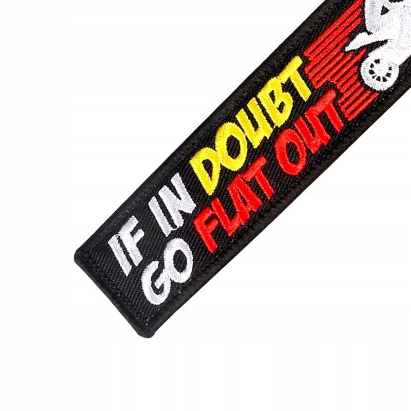 Czarny brelok z napisem \'IF IN DOUBT GO FLAT OUT\' w kolorach białym, żółtym i czerwonym oraz białym motywem motocykla.