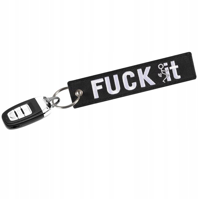 Czarny brelok do kluczy z napisem \'FUCK it\' w białym kolorze, przymocowany do klucza samochodowego.