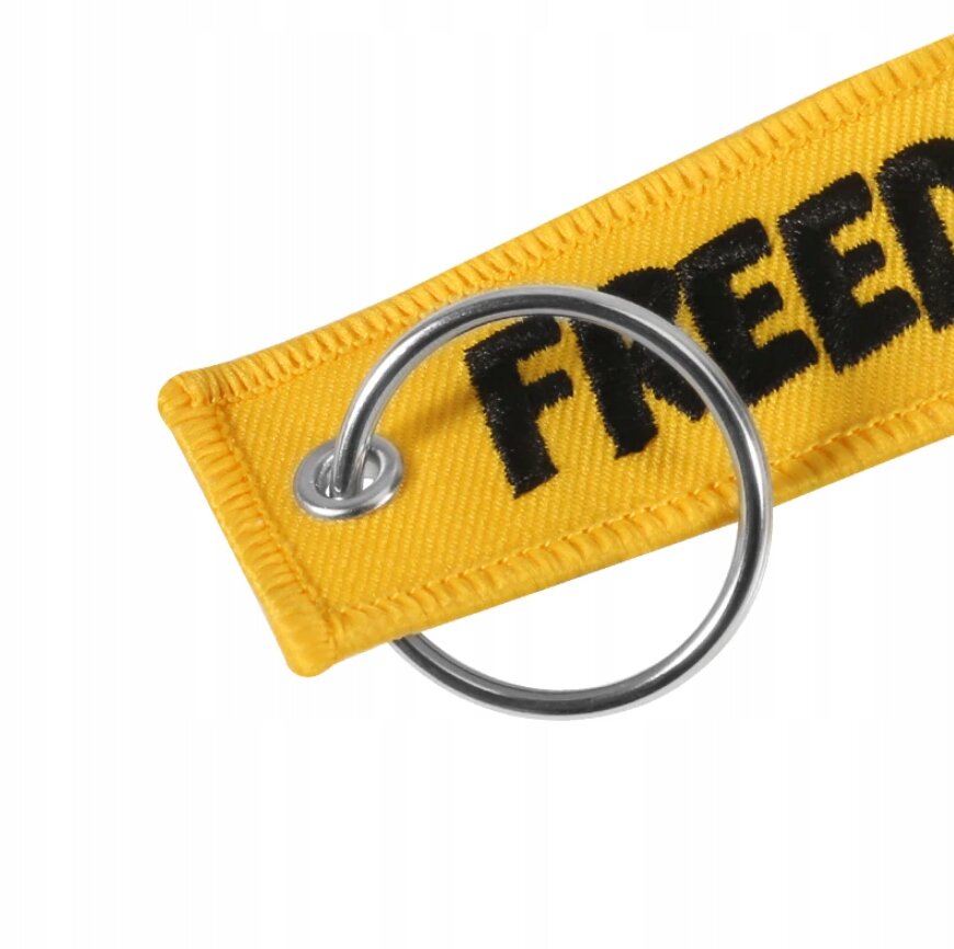 Żółty brelok z metalowym kółkiem, na którym widnieje napis \'FREEDOM\'.