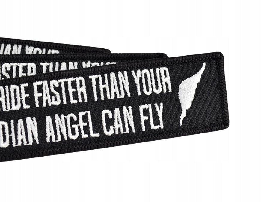 Czarny brelok z białym napisem \'NEVER RIDE FASTER THAN YOUR GUARDIAN ANGEL CAN FLY\' oraz białym symbolem skrzydła.