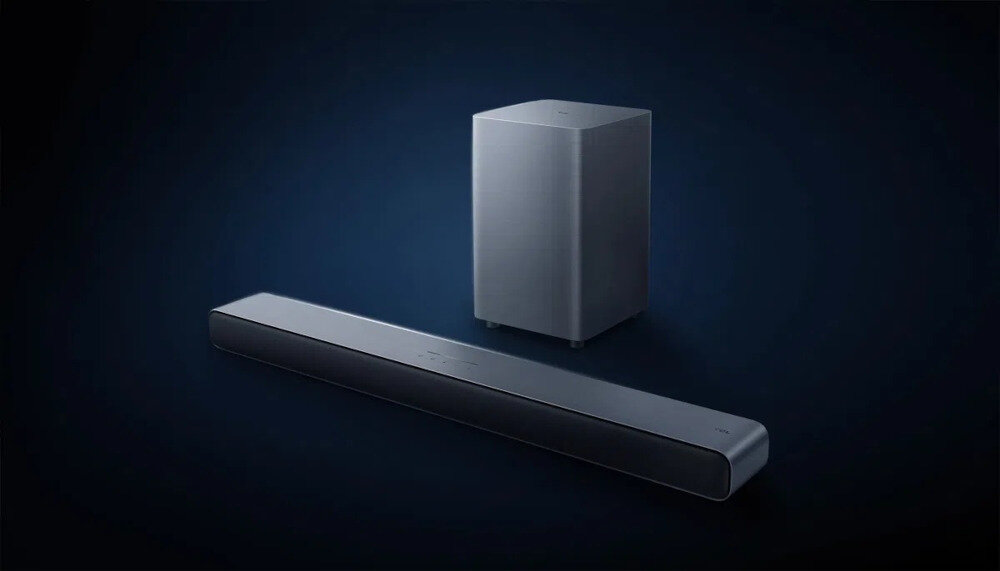 Na ciemnym tle widoczny jest czarny soundbar oraz bezprzewodowy subwoofer. Oba urządzenia mają prosty, nowoczesny design.