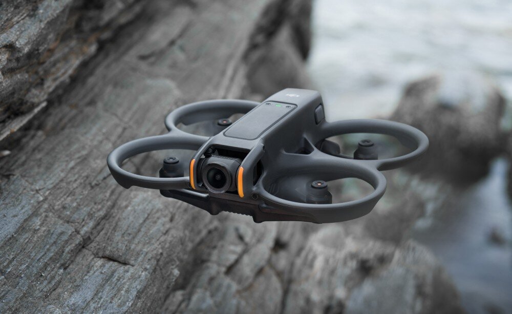 Dron z czterema śmigłami unosi się w powietrzu nad skalistym terenem. Ma kompaktową konstrukcję i kamerę z przodu.