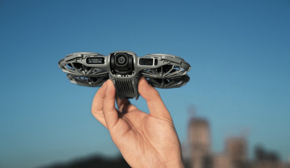 Dron DJI Neo 2 Motion Fly More Combo Osoba trzyma mały dron jedną ręką na tle nieba i rozmytego miasta, przeznaczenie, cechy, zalety