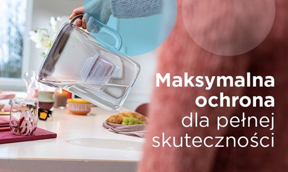 Osoba trzyma dzbanek z filtrem w kuchni, na blacie znajdują się owoce i szklanki. Obok widoczny jest tekst: \'Maksymalna ochrona dla pełnej skuteczności\'.