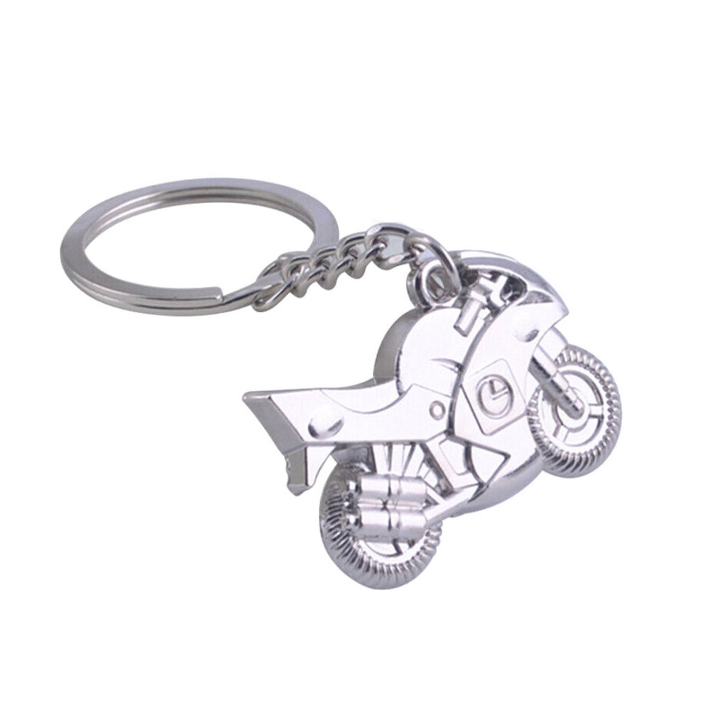 Metalowy brelok do kluczy w kształcie motocykla z detalami takimi jak koła i kierownica. Brelok jest przymocowany do metalowego kółka na klucze za pomocą łańcuszka.
