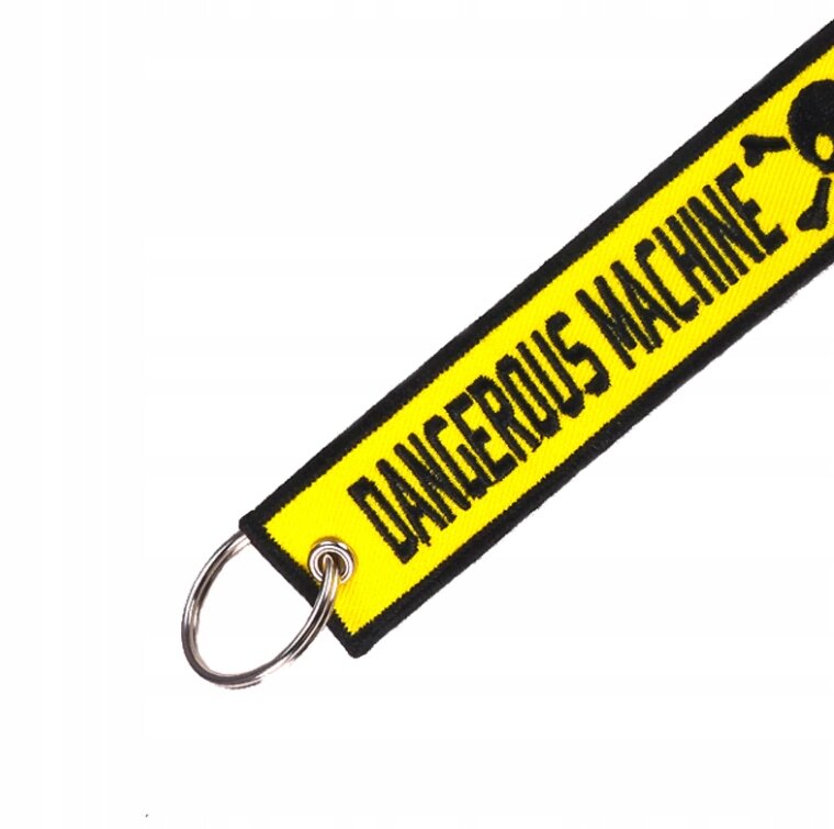 Żółty brelok z czarnym napisem \'DANGEROUS MACHINE\' oraz symbolem czaszki, z metalowym kółkiem do zawieszenia kluczy.