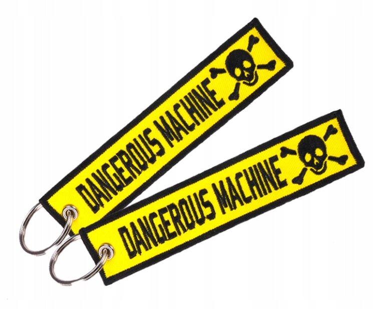 Dwa żółte breloki z czarnym napisem \'DANGEROUS MACHINE\' oraz symbolem czaszki z piszczelami. Breloki mają metalowe kółka do zawieszenia kluczy.