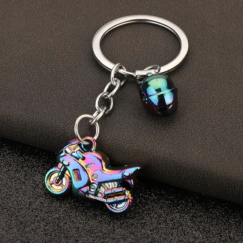 Metalowy brelok w kształcie motocykla i kasku w kolorze neochromowym, przymocowany do okrągłego kółka na klucze. Tło jest ciemne i teksturowane.