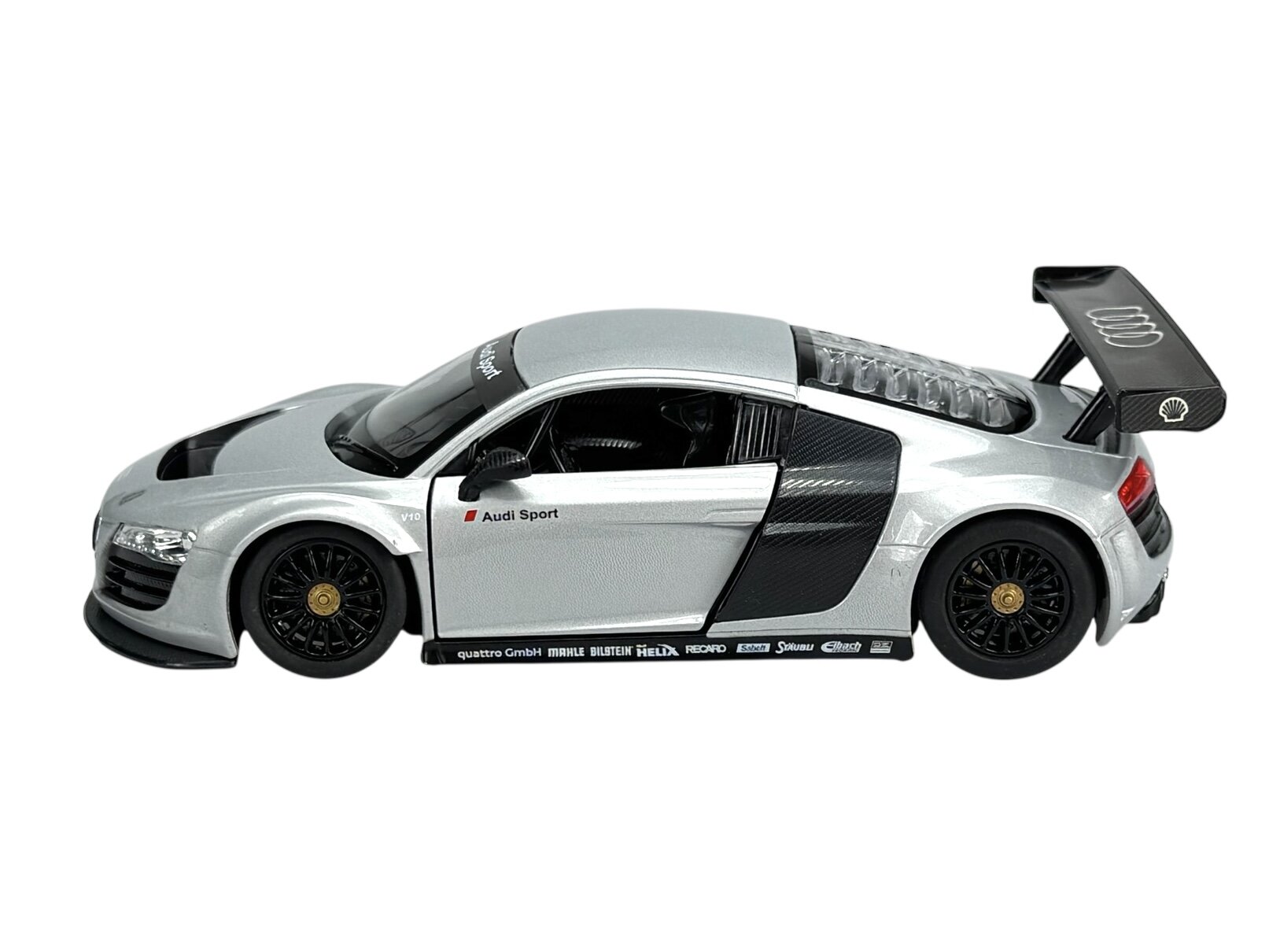 Srebrny model samochodu wyścigowego z czarnymi detalami i dużym tylnym spojlerem. Na boku widoczny napis \'Audi Sport\' oraz różne logotypy na dolnej krawędzi.