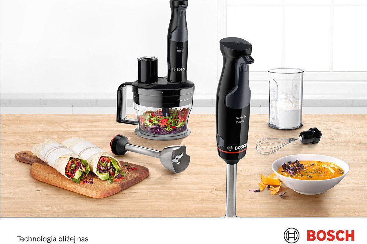 Na blacie kuchennym znajduje się blender ręczny z akcesoriami, w tym pojemnik do siekania i trzepaczka. Obok leży deska z wrapami, a w tle widoczna jest miska z zupą oraz logo BOSCH.