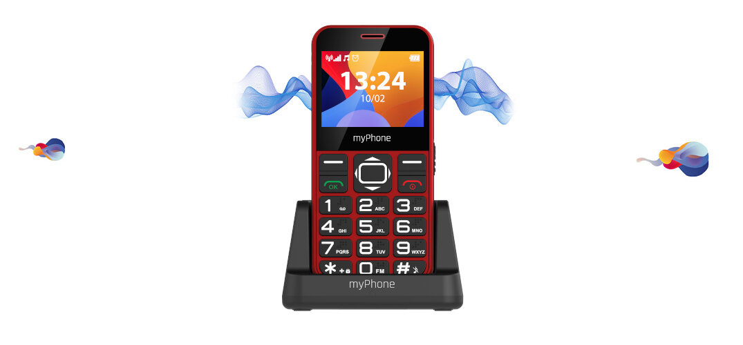 Czerwony telefon z dużymi przyciskami numerycznymi i kolorowym wyświetlaczem, na którym widnieje godzina 13:24 i data 10/02. Telefon umieszczony jest na czarnej podstawce z napisem \'myPhone\'.