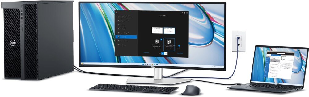 Na obrazie widoczny jest zakrzywiony monitor z dużym ekranem, podłączony do komputera stacjonarnego i laptopa. Na ekranie monitora wyświetlane jest oprogramowanie z ikonami i tekstem, a obok znajdują się klawiatura i mysz.