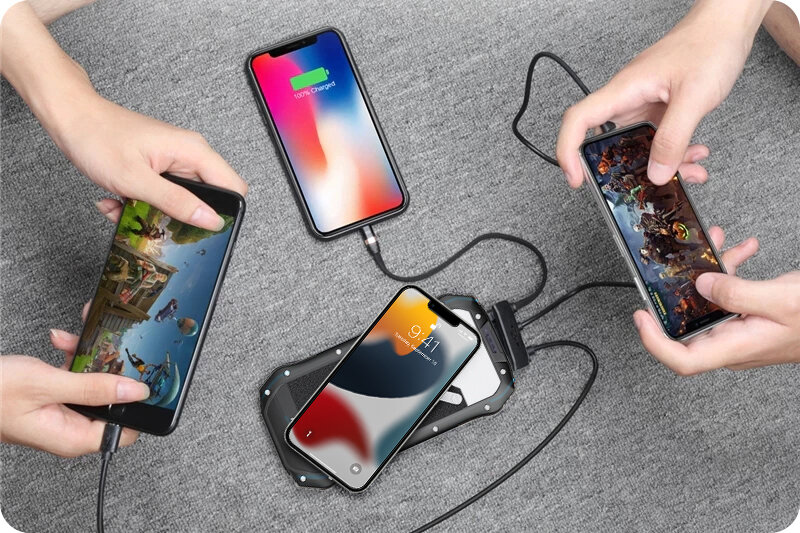 Na szarej powierzchni leży solarny powerbank, do którego podłączone są trzy smartfony. Jeden z telefonów pokazuje ekran ładowania z napisem \'100% Charged\'.