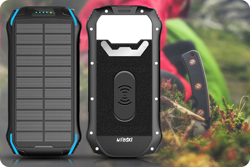Na obrazie widoczny jest solarny powerbank z panelami słonecznymi i ładowarką indukcyjną, z logo \'WEBSKI\'. W tle znajduje się rozmyty krajobraz z roślinnością i nożem.