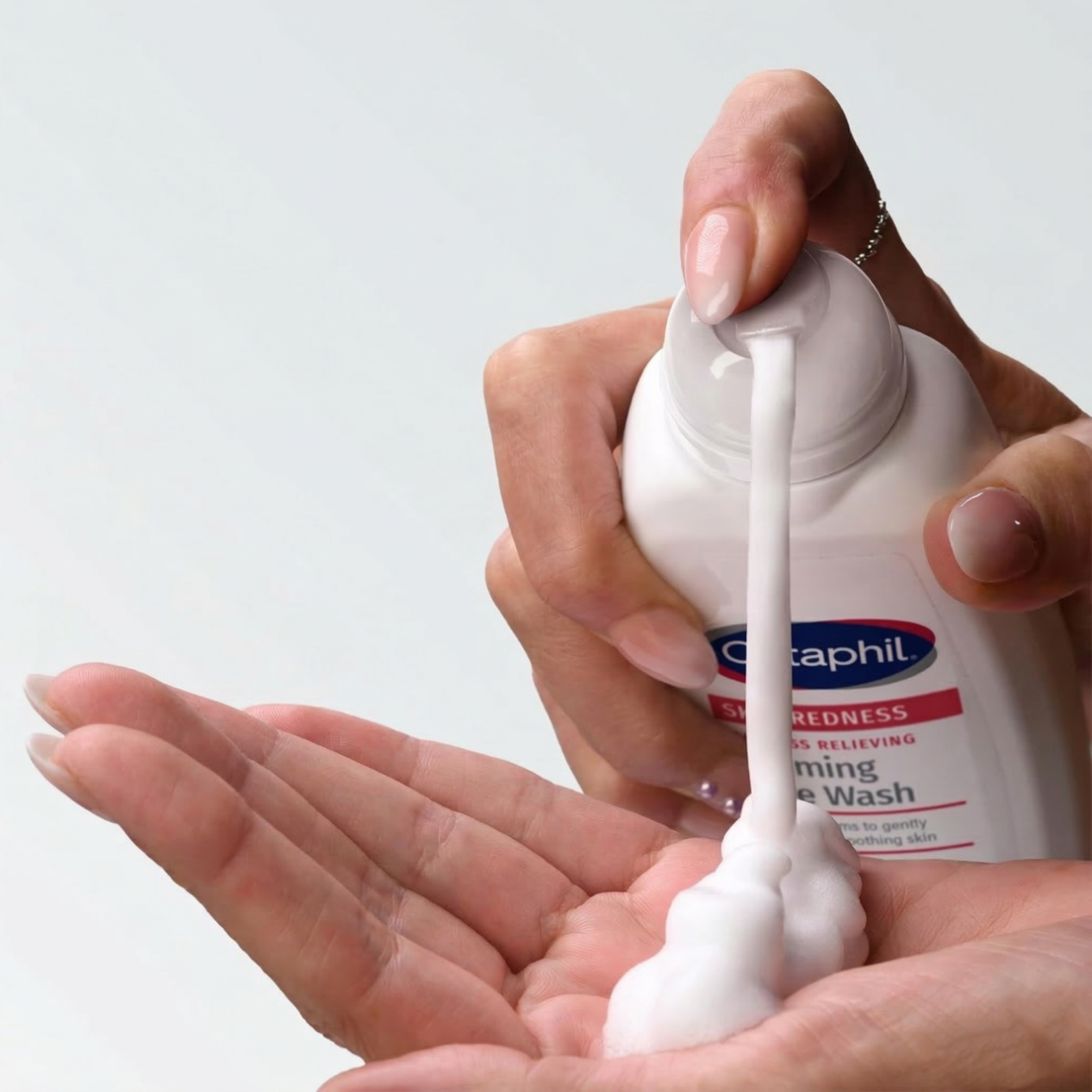 Osoba wyciska piankę z butelki z etykietą \'Cetaphil Skin Redness Foaming Face Wash\' na dłoń. Pianka jest biała i puszysta.