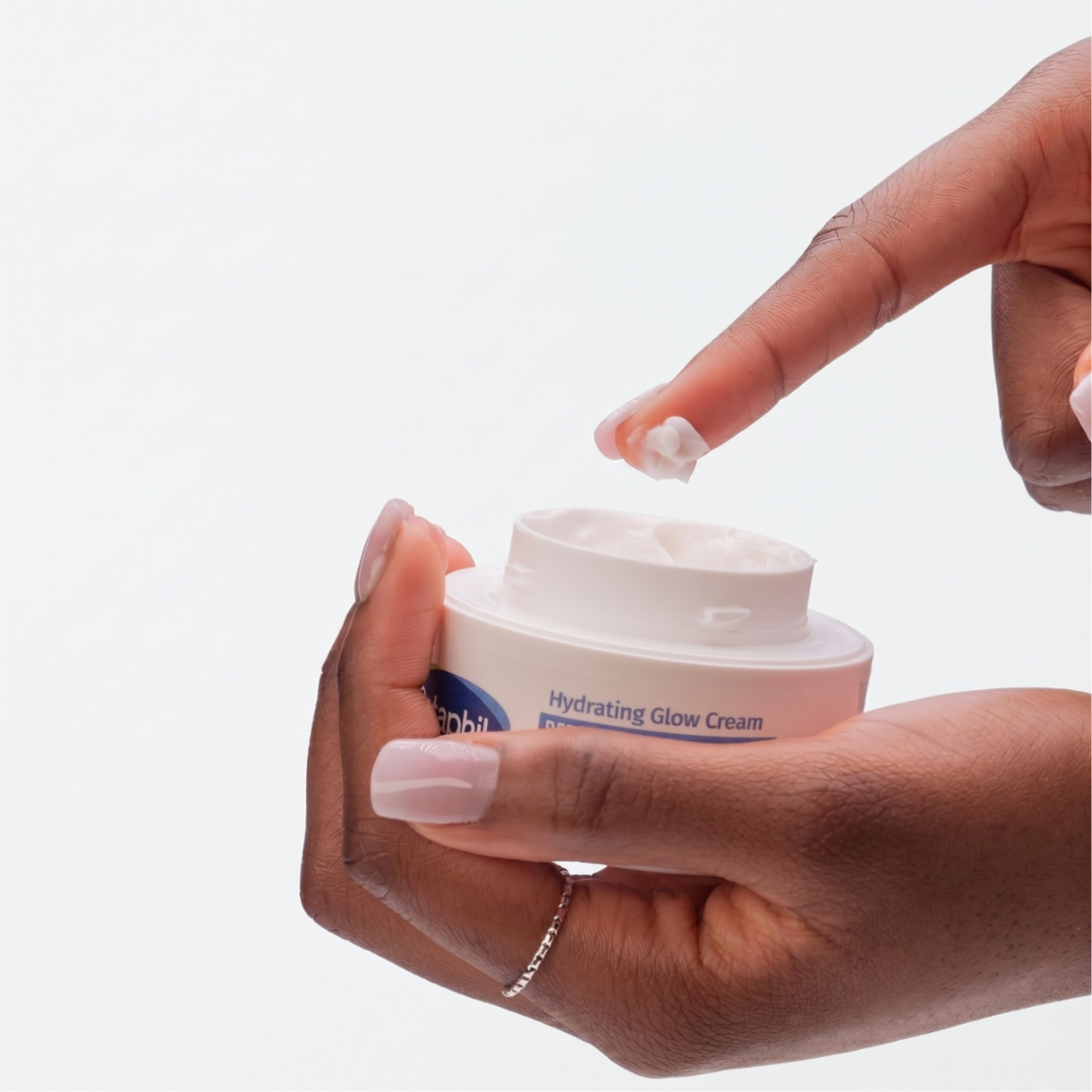 Osoba trzyma otwarte opakowanie kremu z napisem \'Hydrating Glow Cream\'. Na palcu znajduje się niewielka ilość białego kremu.