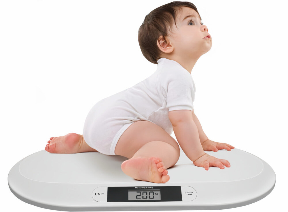 Niemowlę w białym ubranku siedzi na białej wadze elektronicznej. Wyświetlacz pokazuje \'20.0 Kg\'.