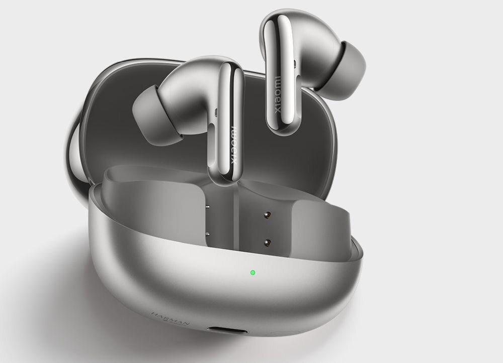 Na obrazie widoczne są białe słuchawki dokanałowe z logo \'XIAOMI\', umieszczone w otwartym etui ładującym. Na etui znajduje się mała zielona dioda.
