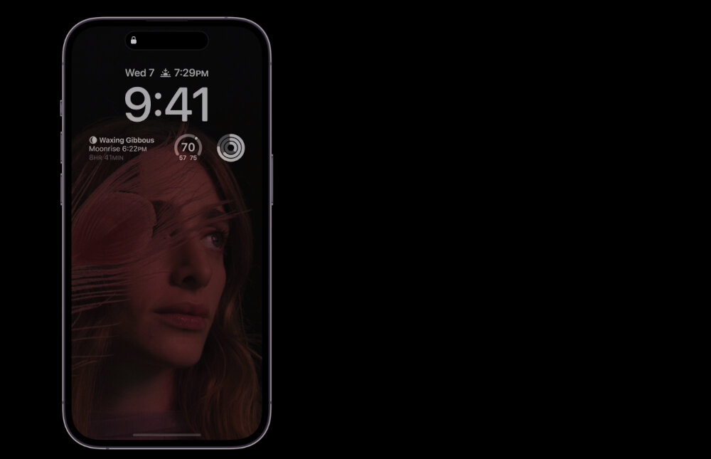 Smartfon z wyświetlaczem pokazującym godzinę 9:41, datę \'Wed 7\', oraz poziom naładowania baterii 70%. Na ekranie widoczna jest twarz kobiety z efektem graficznym oraz informacje o fazie księżyca i pogodzie.