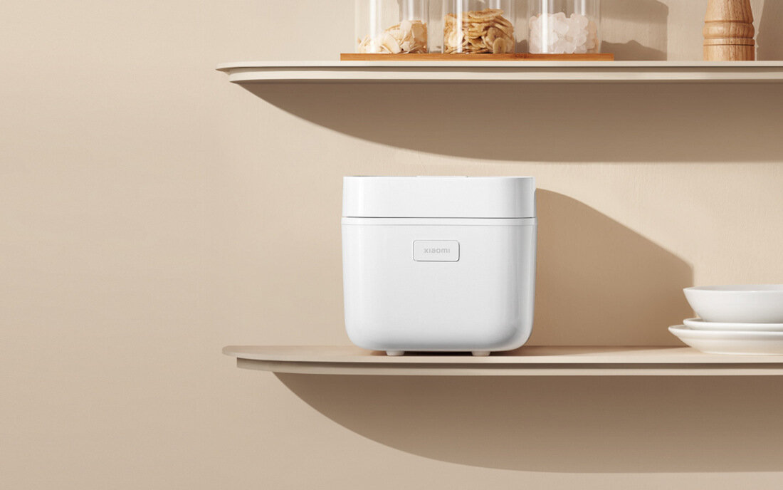 Na półce znajduje się biały ryżowar z logo \'xiaomi\'. Obok widoczne są szklane pojemniki z produktami spożywczymi i biała miska.